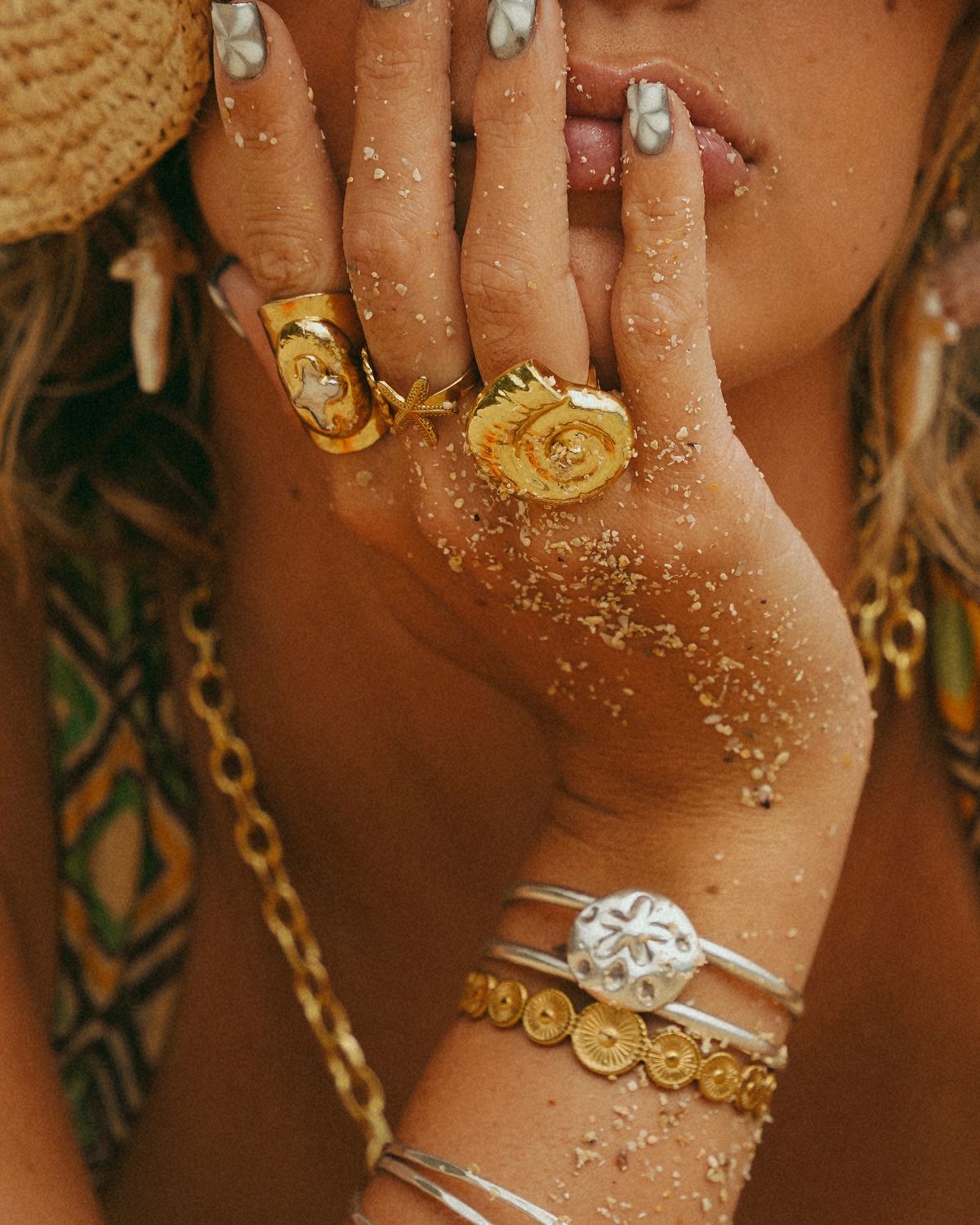 Close-up of woman wearing gold spiral statement ring, starfish ring, stacked gold bands and bangles, styled with a summer drink luxury jewelry trend inspiration by The Jewelry Gossip.