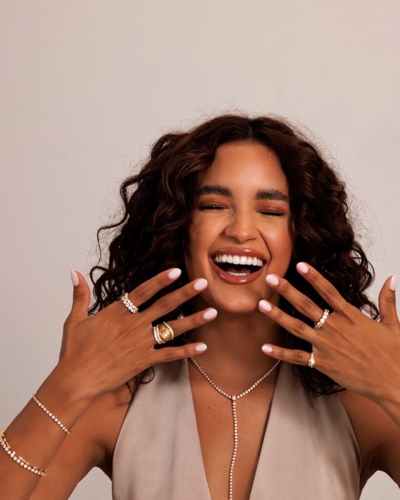 Woman joyfully wearing lab-grown diamond rings, necklace, and bracelets, representing modern sustainable luxury jewelry
