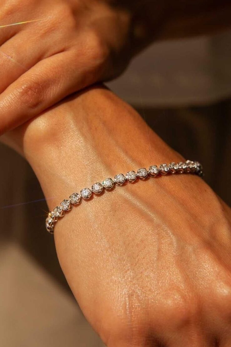 Close-up of hands wearing a diamond tennis bracelet and diamond rings, showcasing fine jewelry sparkle in warm natural light.