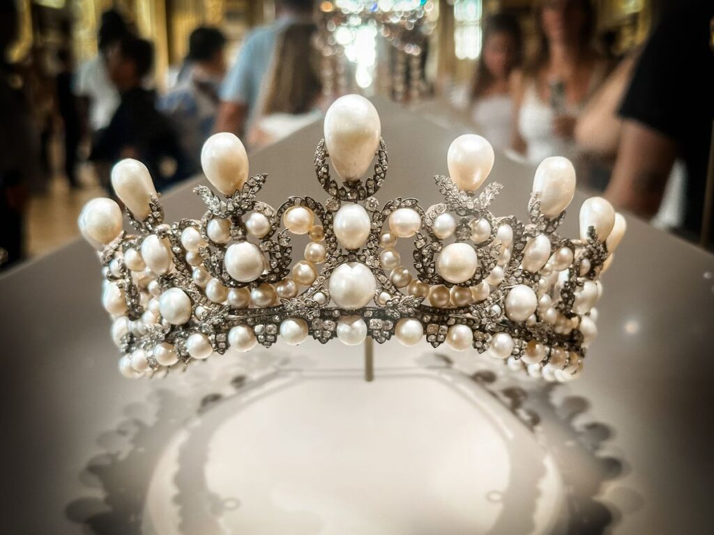 Historic pearl and diamond tiara displayed in a museum setting, featuring layered natural pearls and intricate silver diamond framework, associated with 19th-century French royal jewelry.
