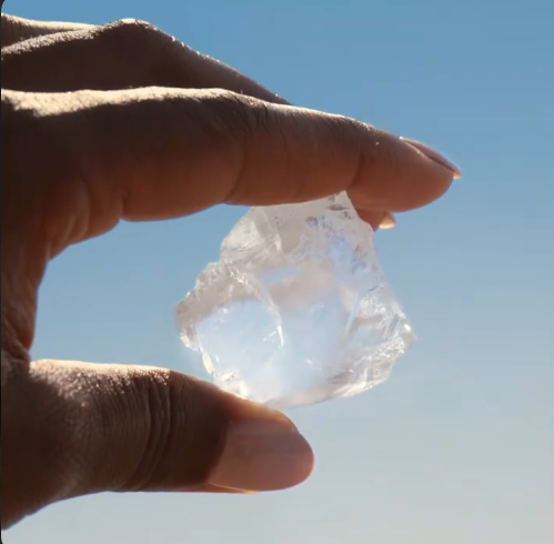 Uncut natural diamond held between fingers against the sky, symbolizing the rarity and natural origin of earth-mined diamonds.