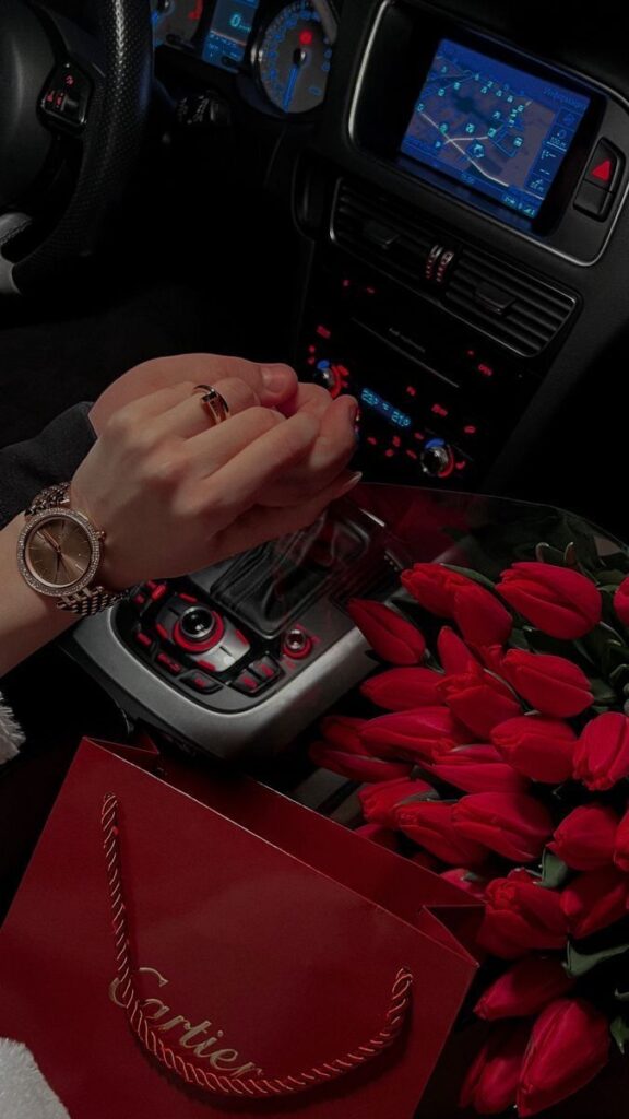 Luxury Valentine’s Day moment featuring a Cartier shopping bag, red roses, and a ring held inside a car, reflecting how high-end jewelry brands associate love with gifting.
