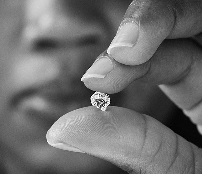  Raw diamond held between fingers showing the beginning of the jewelry supply chain from mining to finished jewelry

