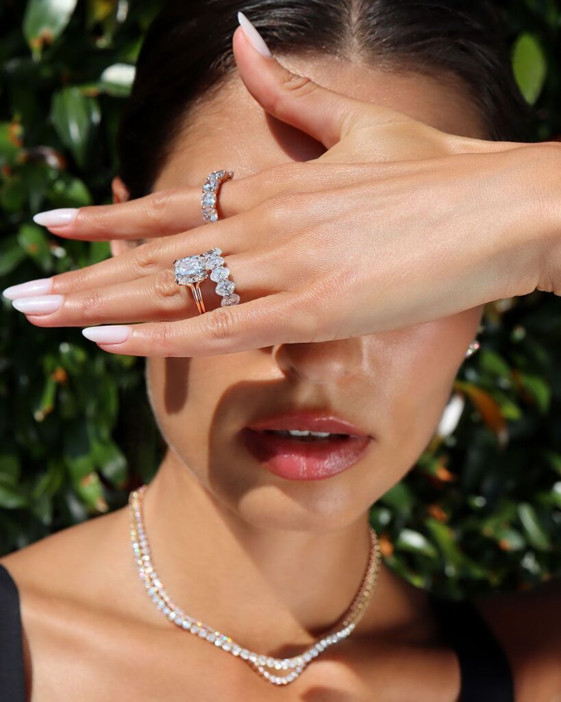 Woman wearing layered lab-grown diamond jewelry including earrings, rings, necklaces, and a diamond tennis bracelet for a modern luxury look.